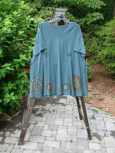 1993 Vagabond Dress Metallic Pinwheel Grey Green OSFA displayed on a swinger, showcasing a rolled V-shaped neckline, A-line shape, and large pinwheel-themed paint accents.