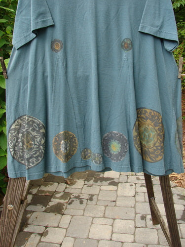 1993 Vagabond Dress Metallic Pinwheel Grey Green OSFA featuring a rolled V-shaped neckline, A-line shape with V inserts, and a sweeping lower hem with a metallic pinwheel pattern.