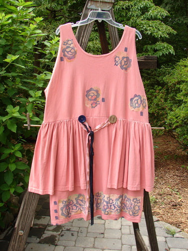 1992 Peplum Dress Floral Border Pink Clover OSFA displayed on a clothes rack, showcasing its empire waistline, oversized vintage buttons, gathered lower section, and hand-dyed silk ribbon accents.