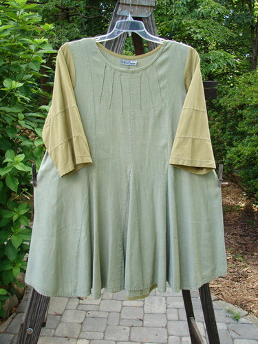 Barclay Playdate Sunrise Spin Dress Unpainted Spice Size 1 on a wooden swing, showcasing its rolled neckline, sectional skirt panels, and multi-insert hemline with contrasting sleeve fabrics.