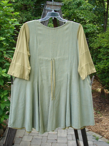 Barclay Playdate Sunrise Spin Dress Unpainted Spice Size 1 displayed on a clothes rack, showcasing its rolled neckline, sectional skirt panels, and sweeping lower shape.