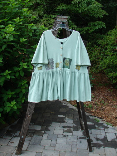 1992 Studio Cardigan Dress Fish and Flower Green Tourmaline OSFA displayed on a swinger, features a flouncy front, gathered waistline, vintage buttons, and a Blue Fish signature patch.