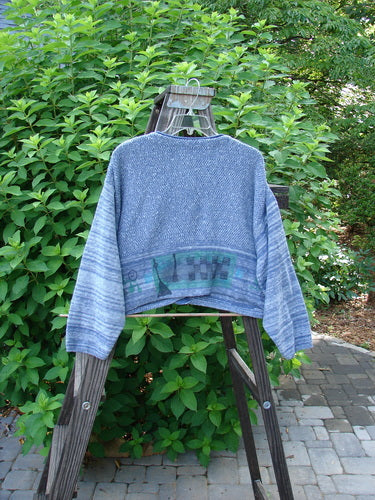 1994 Crop Cardigan Sweater Wine Bottle Haiku Blue OSFA displayed on a swing outdoors, showcasing its unique texture, dual contrasting knits, and stoneware buttons against a garden backdrop.