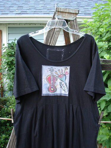 1992 Patched Little Storma Dress Music Black Small OSFA features a black shirt with a guitar and trumpet drawing, tapering lower, deep rounded neckline, gathered top rear, and vintage music-themed patches.