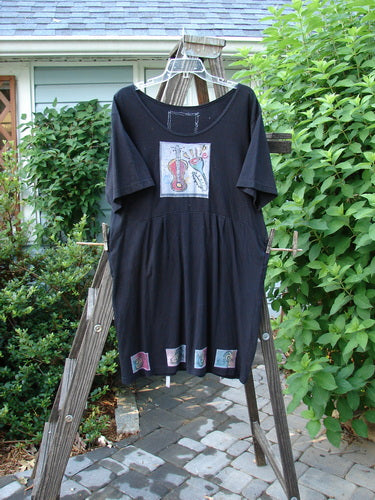 1992 Patched Little Storma Dress Music Black Small OSFA displayed on a wooden ladder, showcasing a deep rounded neckline, gathered top half rear, and music-themed patches.