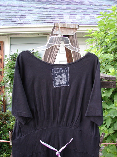 1992 Patched Little Storma Dress Music Black Small OSFA on clothes rack, featuring a white flower and music-themed patches, with a deep rounded neckline and gathered back.
