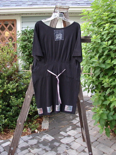 1992 Patched Little Storma Dress Music Black Small OSFA displayed on a wooden rack with a tie waist, deep rounded neckline, and vintage music-themed patches.