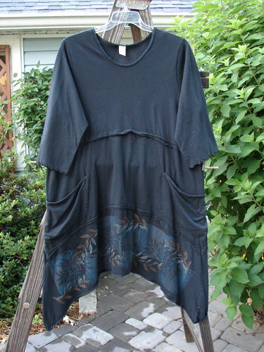 Barclay Reverse Stitch Double Pocket Tunic Dress Fern Garden Black Size 2, hanging on a clothesline, showcasing exterior horizontal flutter seams and two drop front wrap-around exterior pockets with a varying hemline.