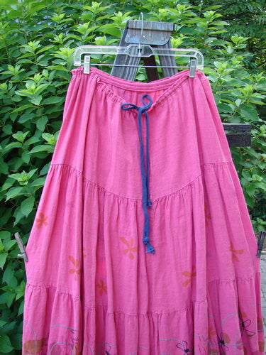 Barclay Linen Drawstring Ruffle Skirt Daisy Fence Flamingo Size 2 displayed on a rack, featuring a full drawstring waistline, alternating seams, and fringe edges, capturing its billowy A-line shape.