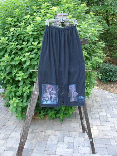 1997 Indra Skirt Whimsical Forest Obsidian Size 1, featuring a whimsical tree and house drawing, deep side pockets, colorful buttons, and an elastic waist, displayed on a rack.