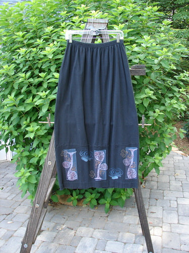 1997 Indra Skirt Whimsical Forest Obsidian Size 1 on a rack, featuring a full elastic waistline, double-paneled lower, colorful buttons, deep side pockets, and sweet loop closures.