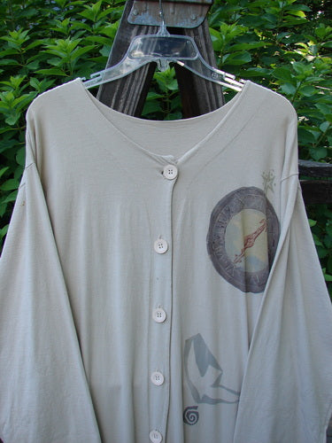1994 Column Dress Belief Mist Size 1 displayed on a hanger outdoors, showcasing its long sleeves, full front button design, and V-shaped neckline with a flounced bottom.
