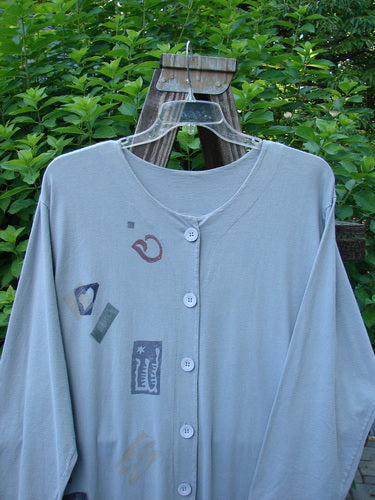 1994 Column Dress Heart Solstice Blue Size 1: A grey shirt with stickers on it. Full front button duster type shape with elongating paint in the 1994 theme. Kick flounce and v-shaped neckline. Longer sleeves and back u-shaped upper shoulder seam.