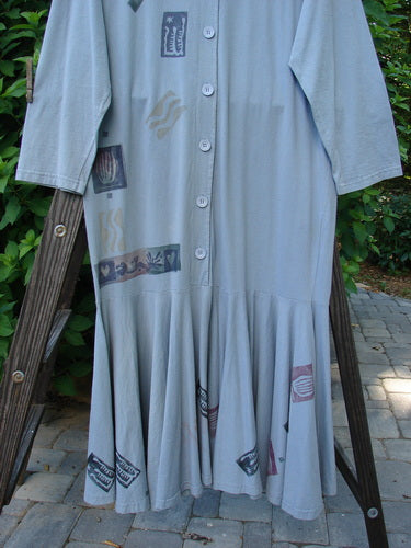 1994 Column Dress Heart Solstice Blue Size 1 displayed on a wooden ladder. Features a V-shaped neckline, long sleeves, full front buttons, and an abundant heart-themed paint design.