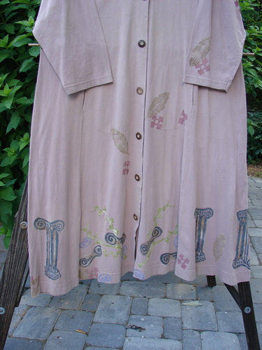 1993 Modernismo Duster Dress Columns Ash Pink OSFA, hanging on a clothesline, showcasing vintage column and leaf patterns, wooden buttons, front pockets, scooped neckline, and a flowing hemline.