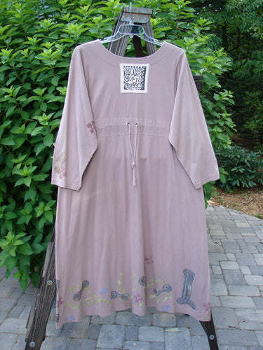 1993 Modernismo Duster Dress Columns Ash Pink OSFA displayed on a rack, showcasing vintage wooden buttons, kangaroo pockets, a scooped neckline, and a sweeping lower with column and leaf patterns.