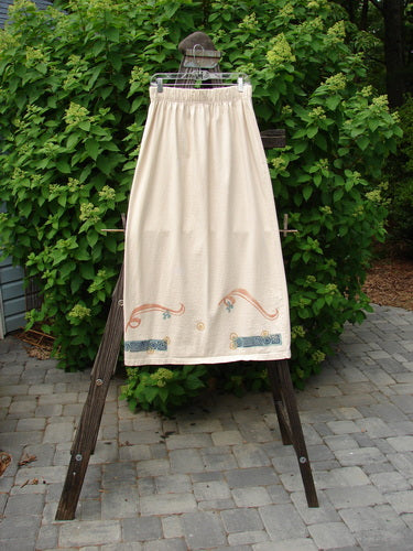 1995 Kick Skirt Resort Travel Champagne Size 2 displayed on a wooden rack, showcasing a full elastic waist and sassy rear kick pleat, with travel-themed painted accents and an elongating shape.