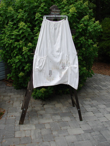 2000 Side Pocket Skirt Summer Treat White Size 2 displayed on a wooden clothes rack, featuring a full elastic waist, elastic-edged side pocket, and vertical panels for a flowing, draped look.