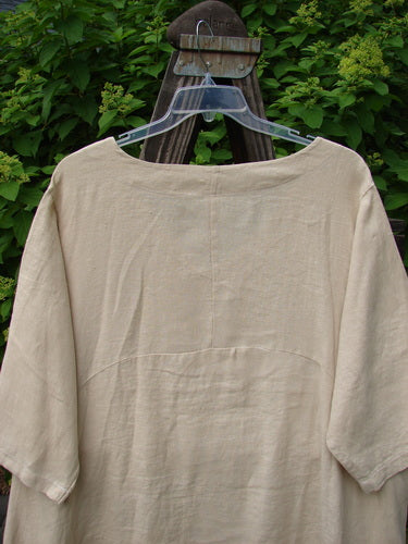 Barclay Linen Urchin Side Pocket Tunic Dress Unpainted Dried Wheat Size 2 displayed on a wooden stand, featuring a wide V-shaped neckline, three-quarter sleeves, and two exterior drop pockets.