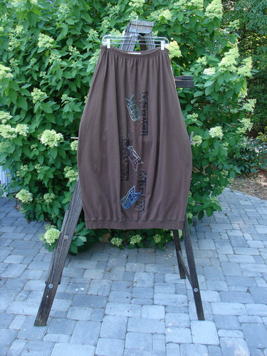 1996 Thermal Whimsical Skirt Tribal Molasses Size 2 displayed on a wooden rack, featuring an elastic waistline, ribbed hem, vertical panels, abstract tribal paint, and deep side pockets.