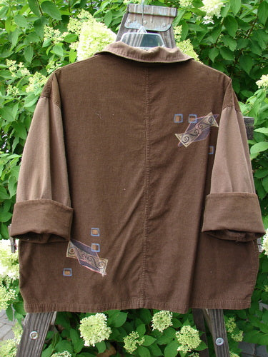 1997 Corduroy Mason's Jacket Structural Lumber OSFA: Brown jacket with patch, folded neckline, front painted pockets, cuffed cord sleeves, metal buttons, and riveted pocket edges. Swirl paint in structural home theme.