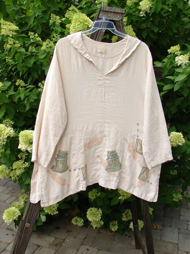 1999 Linen Antique Top Baker Tea Dye Size 1 on a hanger, showcasing its V neckline, rounded collar, hidden pockets, and unique painted design.