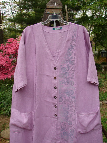 Barclay Linen Double Tie Back Jacket Garden Side Lilac Size 2 displayed on a hanger, highlighting its deep V neckline, A-line sweep, vertical stitchery, front drop pockets, and garden-themed paint detailing.