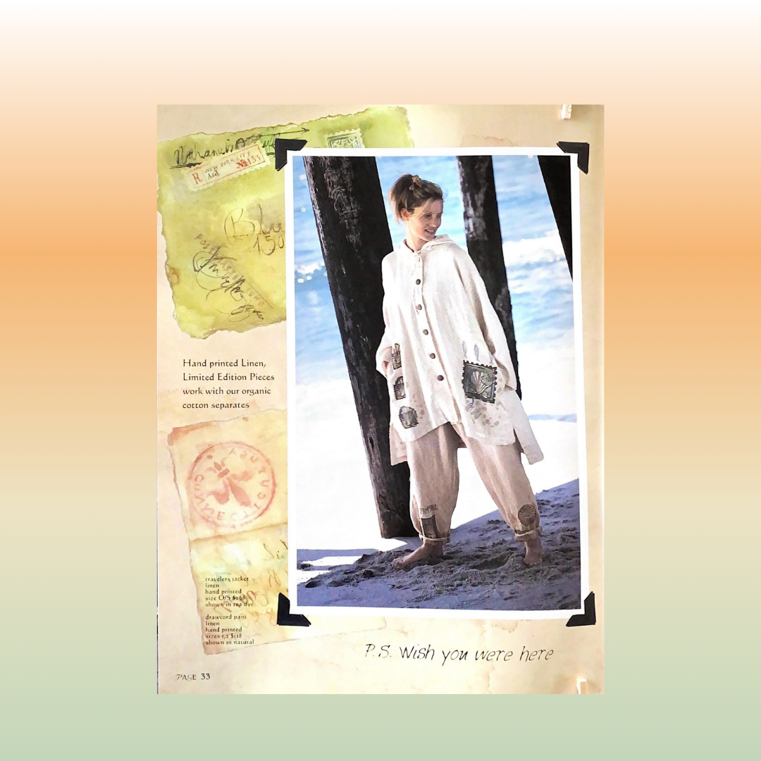 A woman standing on a beach wearing a natural Hooded Cardigan, next to a Boardwalk pillar. A close-up of a paper mailing stamp is on the Cardigan representing the Travel Theme from 1998 Resort collection