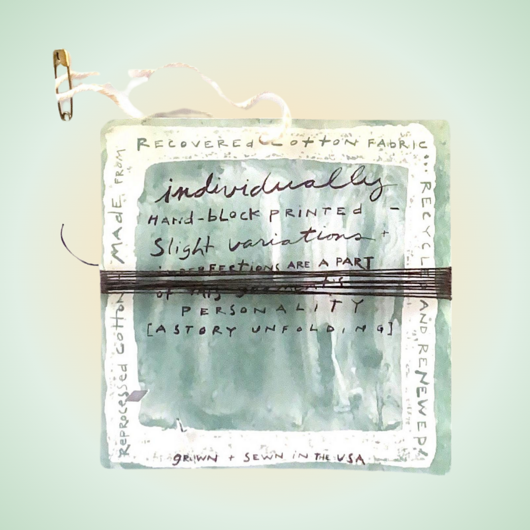 A close-up of a clothing paper hang tag advertising individuality in clothing. Twine wraps the middle in contrasting black. A twine string with a tiny clothespin is attached to the top in a closed position. Gradient pastel backdrop in yellow and Greens