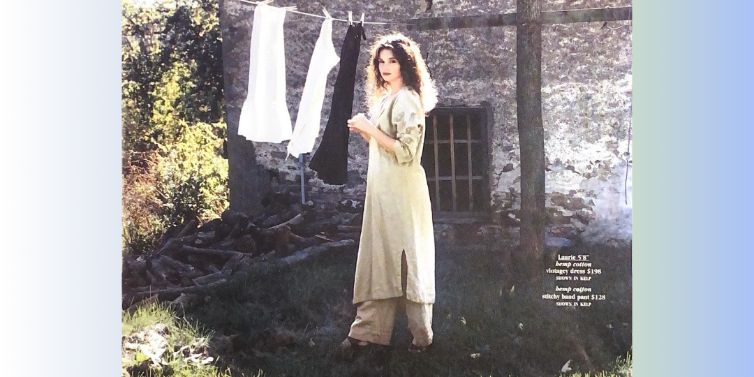 A woman stands in a grassy sunny area hanging clothing on a line. The shadows create a juxtaposition in mood and theme. A stone home is in the background with a wooden framed windows. She is exhibiting 2001 spring clothing for BFC last year.
