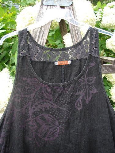Bluefishfinder.com Barclay Summercloth Lace Two Pocket Pinafore Moody Night Bloom Black Size 0, a black sleeveless pinafore with a lace-trimmed neckline and faint moody night bloom floral print. The lightweight woven fabric hangs in a loose A-line shape, draped over a rustic wooden hanger among pale flowers and green leaves.