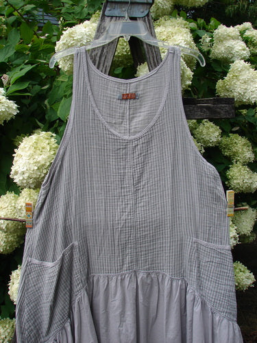 Barclay Gauze Batiste Summer Frock Jumper Stripe Light Stone Size 1, a light stone-gray sleeveless dress in fine striped gauze batiste with a scoop neckline and gathered skirt. It hangs on a clear hanger against white hydrangeas and dark wood.