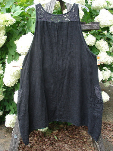 Bluefishfinder.com Barclay Summercloth Lace Two Pocket Pinafore in Moody Night Bloom black, Size 0, with a lace yoke and two side pockets. The dark, softly textured pinafore hangs from a wooden ladder against white hydrangeas, its loose A-line shape and gathered side panels clearly visible.