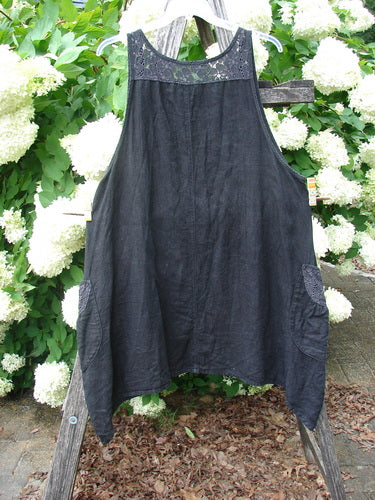 Bluefishfinder.com Barclay Summercloth Lace Two Pocket Pinafore Moody Night Bloom Black, size 0, is a loose black pinafore with a lace-trimmed neckline and two side pockets. Its softly draped fabric hangs from narrow straps, set against bright white hydrangeas and green foliage.