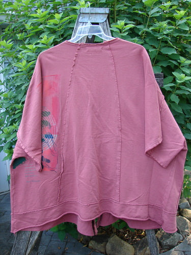 Barclay NWT Photogram Open Front Jacket Walt Whitman Script Desert Rose OSFA displayed outdoors on a hanger, showcasing its wide three-quarter sleeves, open front, and angular hem with raw edges.