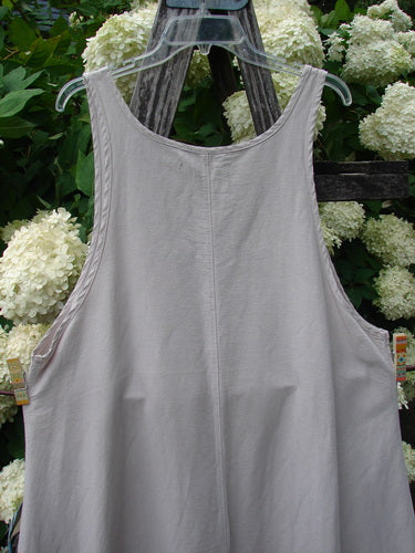 Barclay Hemp Silk Everyway Pinafore in unpainted palest peach, size 1, shown as a sleeveless garment with a wide scoop neckline and softly draped A-line shape. The hemp-silk fabric has a matte, lightly textured finish and hangs from a clear hanger against white hydrangeas and dark wood.
