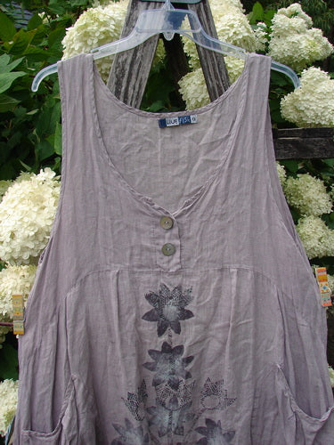 Bluefishfinder.com Barclay Linen Tuesday's Dress Majestic Petal Mallow, a size 0 sleeveless linen dress in soft mauve-gray. It has a curved neckline, two front buttons, and a gathered skirt panel with dark floral print, hanging on a clear plastic hanger.