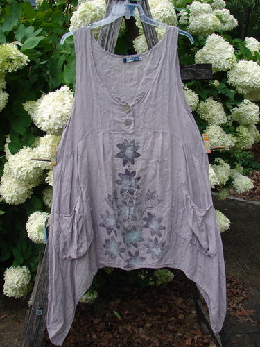 Bluefishfinder.com Barclay Linen Tuesday's Dress Majestic Petal Mallow size 0 in soft mauve linen, a loose sleeveless dress with a scoop neckline, two front buttons, and a faded floral print down the center. It hangs on a clear hanger against white hydrangeas and dark greenery.