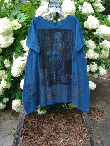 Barclay NWT Textured Gauze Chaya Tunic Window Meditation in indigo, Size 1, hangs from a wooden stand. The loose gauze top has short sleeves, a round neckline, and a sheer black graphic panel across the front, set against white hydrangeas and greenery.