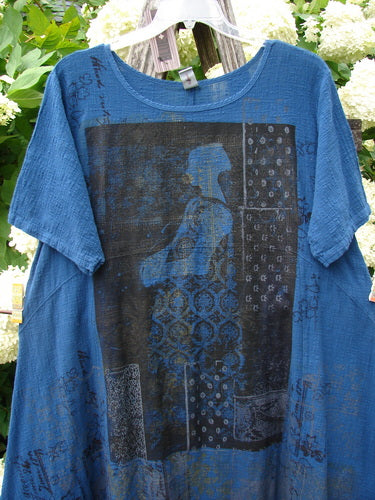 Barclay NWT Textured Gauze Chaya Tunic in indigo, size 1, with a loose short-sleeve silhouette and a round neckline. The semi-sheer gauze fabric is printed with layered black and blue meditation window motifs, hanging against a floral backdrop.