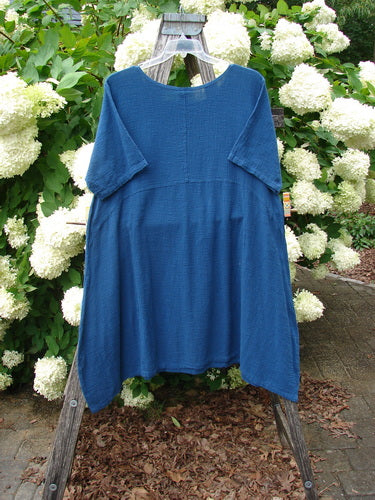 Barclay NWT Textured Gauze Chaya Tunic Window Meditation in indigo, Size 1, hangs from a wooden ladder and shows a loose, airy silhouette with short wide sleeves and a softly textured gauze finish. The deep blue fabric stands out against white hydrangeas and green foliage.