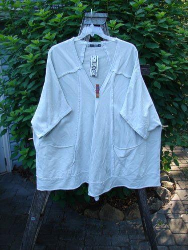 Barclay NWT Photogram Open Front Jacket Unpainted Dew OSFA displayed on a hanger outdoors, showcasing its wide three-quarter sleeves, open front, angular hem, raw edges, and dolman shoulders.