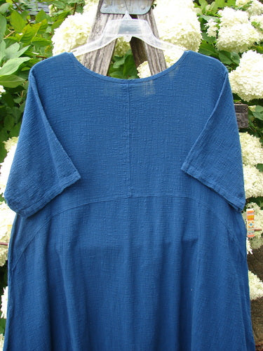 Barclay NWT Textured Gauze Chaya Tunic Window Meditation in indigo, size 1, with a softly crinkled gauze texture, wide short sleeves, and a simple rounded neckline. The tunic hangs on a clear hanger against leafy white flowers, its deep blue fabric falling in a relaxed, airy drape.