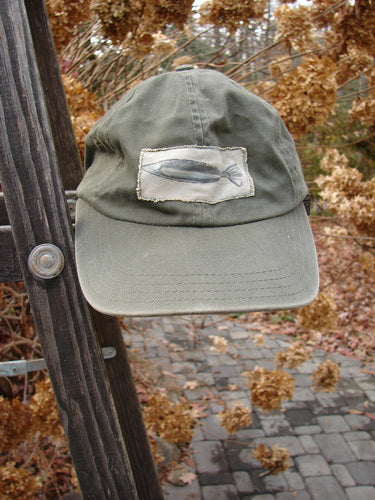 1999 Patched Men's Baseball Cap with Fish Logo. Forest green hat on a ladder. Close-up of hat with a patch. Adjustable strap.