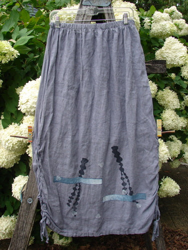 Bluefishfinder.com 1997 Breeze Skirt Sealife Naya Size 1 in soft gray fabric, a loose skirt with a gathered waistband, side ties, and dark sealife motifs near the hem. It hangs centered against white hydrangea blooms and greenery, with a muted, natural outdoor backdrop.
