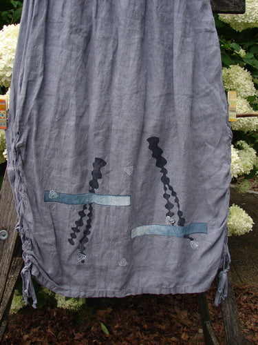 Bluefishfinder.com 1997 Breeze Skirt Sealife Naya Size 1 in gray, made from softly crinkled fabric with a loose drape and tasseled hem. Black and blue sealife motifs sit near the lower front, set against an outdoor floral backdrop.