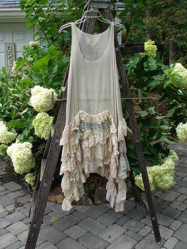 Magnolia Pearl Linen Voile Ruffle Pinafore Gray Silver Pastels OSFA draped on a wooden ladder amidst a garden setting.