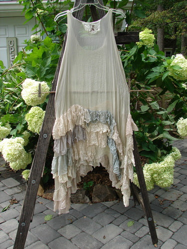 Magnolia Pearl Linen Voile Ruffle Pinafore Gray Silver Pastels OSFA displayed on a wooden ladder amidst a garden, showcasing its elegant ruffles and floral design.