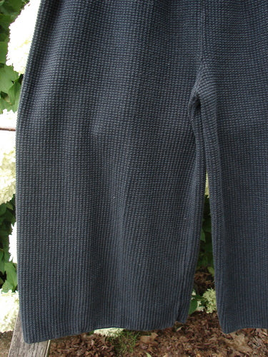 Bluefishfinder.com 1993 Thermal Waffle Wide Leg Crop Pant in unpainted black, size 1, shown in a close-up of textured waffle-knit fabric with a wide leg and cropped hem. The dark, ribbed surface falls in soft vertical folds against a leafy outdoor backdrop.