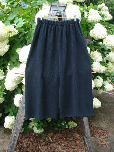 Bluefishfinder.com 1993 Thermal Waffle Wide Leg Crop Pant in unpainted black, size 1, hangs from a wooden A-frame outdoors. The wide-leg crop silhouette shows a textured waffle knit and an elasticized waistband, with the dark fabric set against bright white blossoms and green foliage.